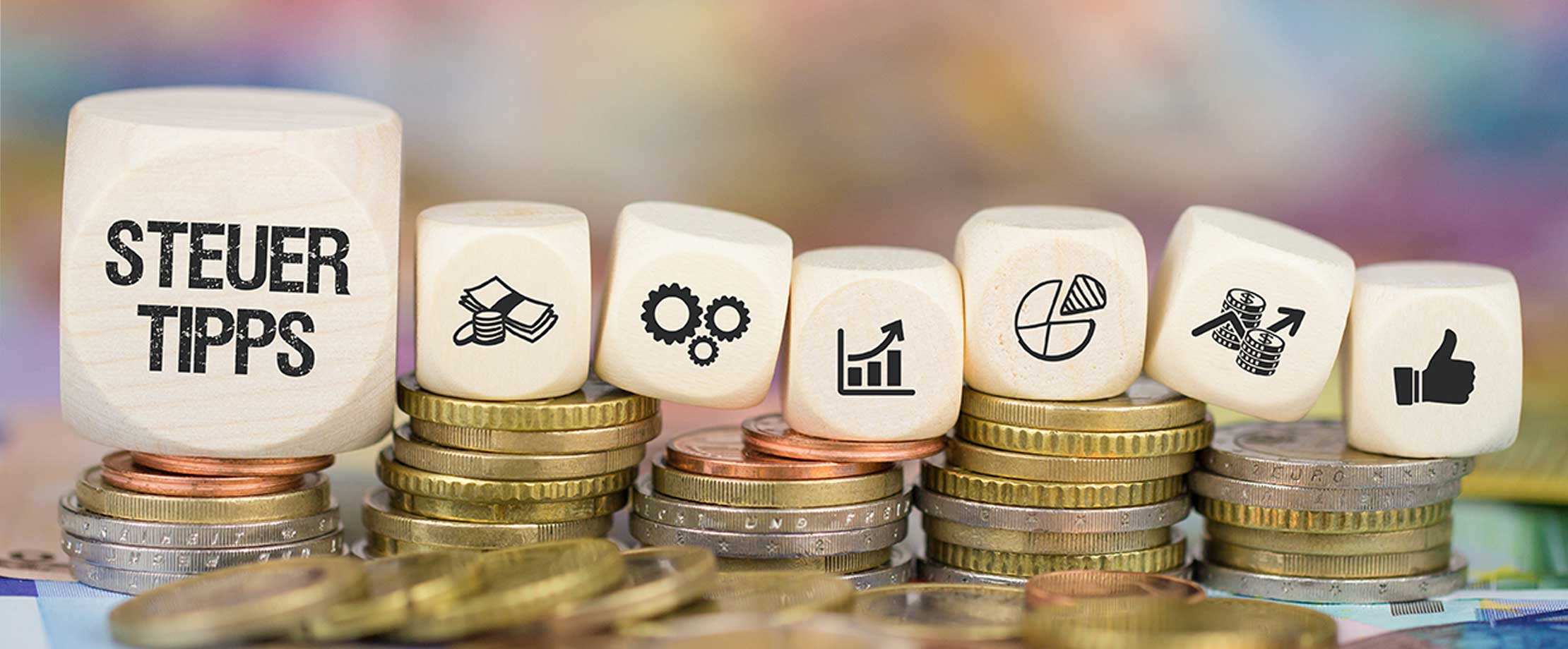 Der Gewinnfreibetrag für Unternehmerinnen und Unternehmer Würfel liegen nebeneinander auf Münzstapeln in verschiedener Höhe. Auf dem Würfel ganz rechts, der am größten ist, steht “Steuertipps”.