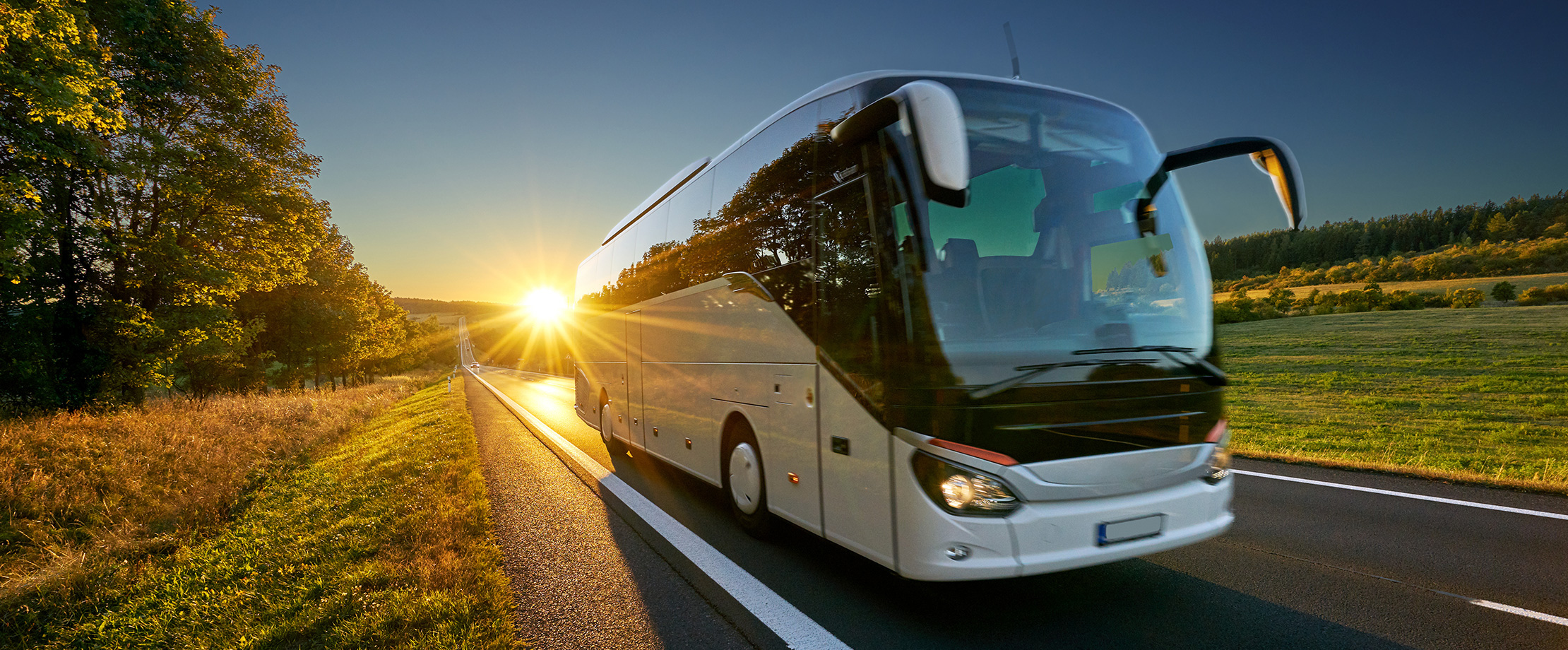 Die beste Firmen-Kfz-Versicherung & Fuhrparklösungen Ein Reisebus auf der Landstraße vor einem Sonnenuntergang.