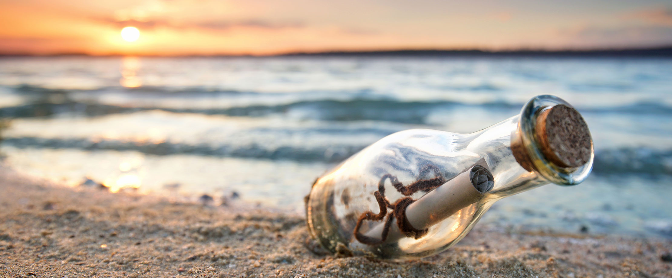 Checkliste: Einreichen Arztrechnungen Eine Flaschenpost wurde am Strand angeschwemmt und liegt im Sand. Im Hintergrund geht die Sonne hinter dem Meer unter. Der Wellengang ist sanft.