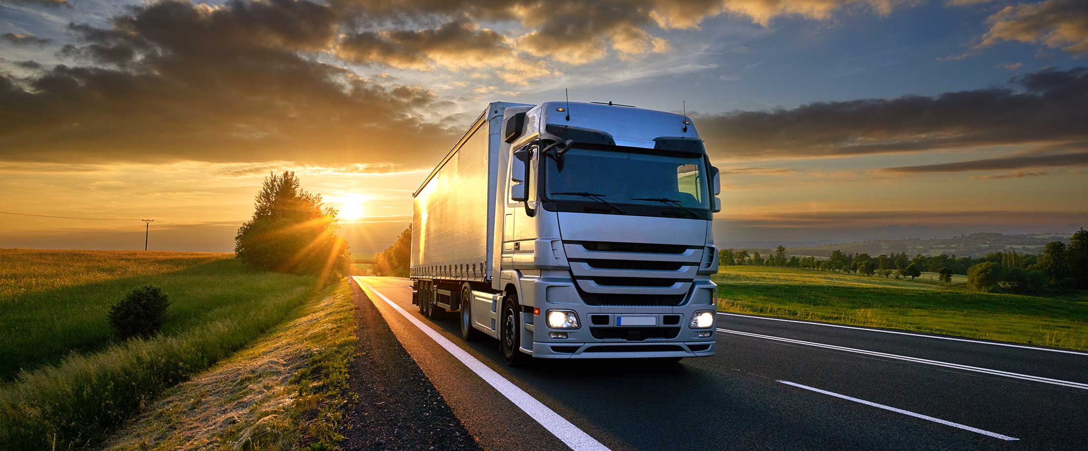 Die beste Lkw-Versicherung Ein weißer Lkw fährt bei Sonnenuntergang eine Straße entlang.