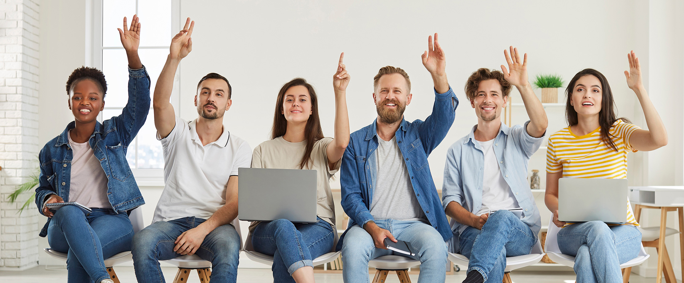 Die beste betriebliche Altersvorsorge Junge Angestellte sitzen nebeneinander auf einer Bank und zeigen auf. Zwei von ihnen haben einen Laptop auf dem Schoß.